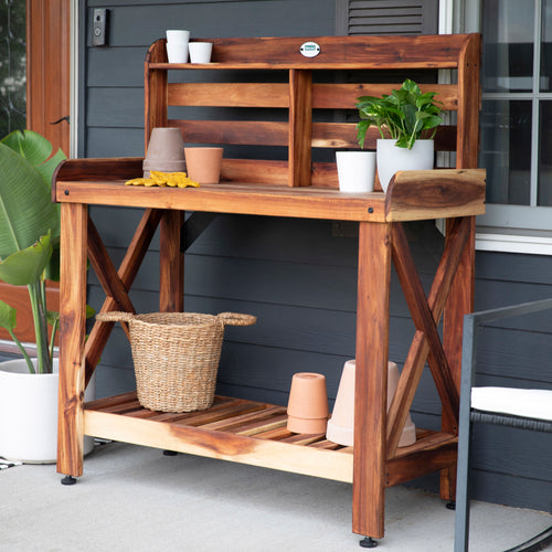 Acacia wood potting bench with a slatted lower shelf set up on an outdoor patio.
