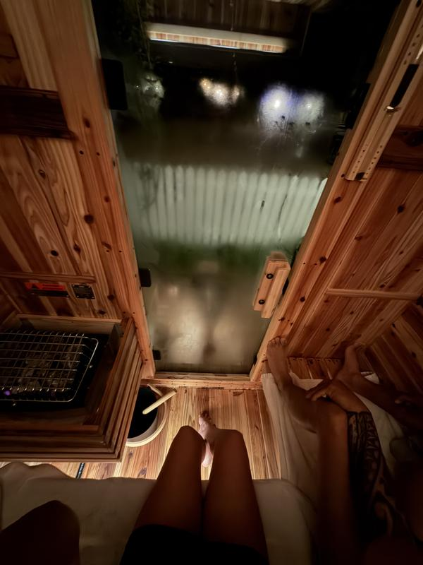 Person standing inside a wooden sauna with a view of a snowy outdoor scene.