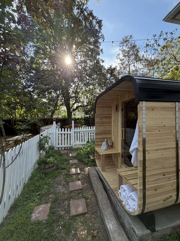 Wooden outdoor shower cabin in a backyard setting with trees and a white fence.