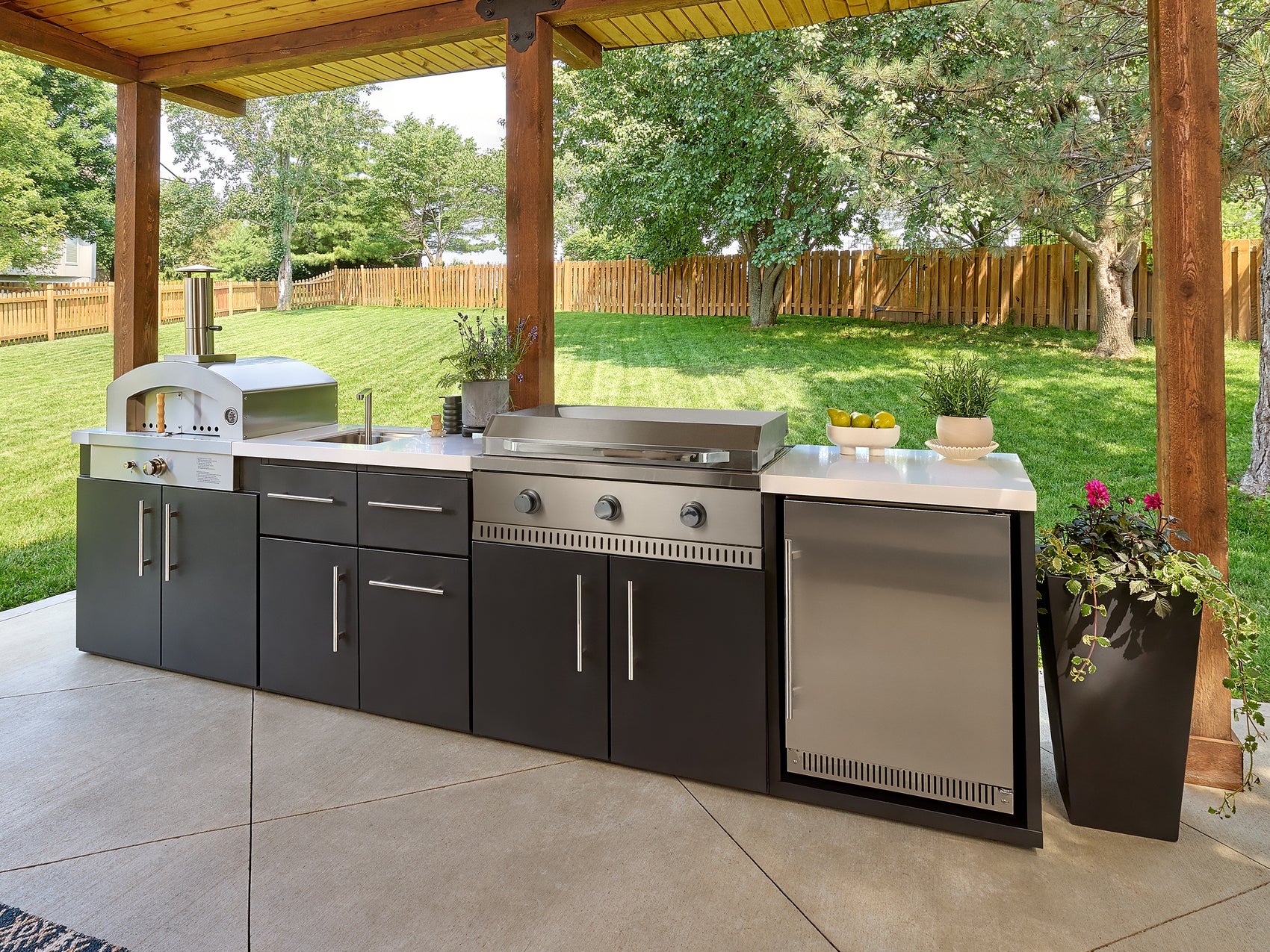 Emory outdoor kitchen with pizza oven, outdoor griddle, sink, and stainless steel fridge set under a covered patio.