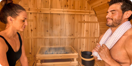 Two people in a wooden sauna with one person holding a towel.