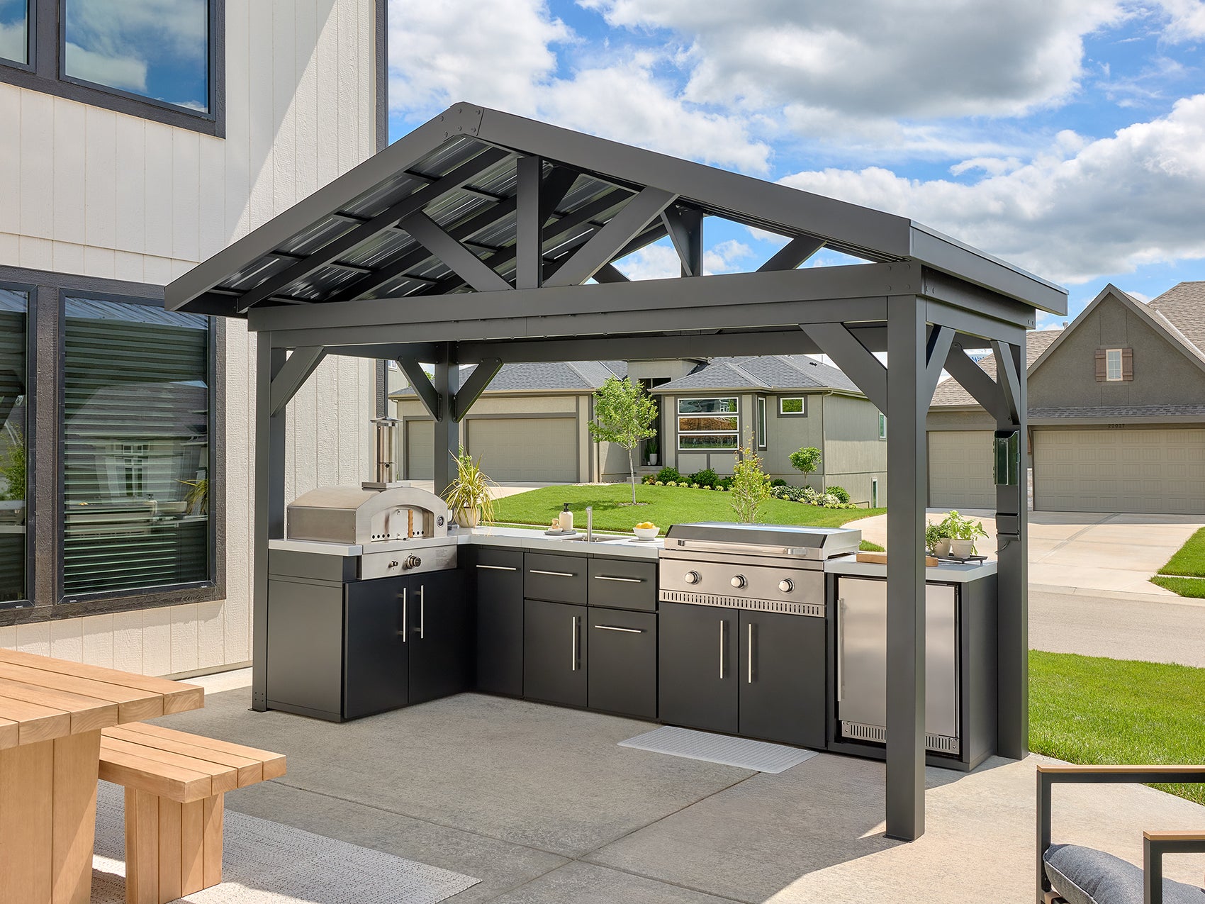 Lancaster L-Shape outdoor kitchen under a galvanized steel roof with a pizza oven, griddle, sink.