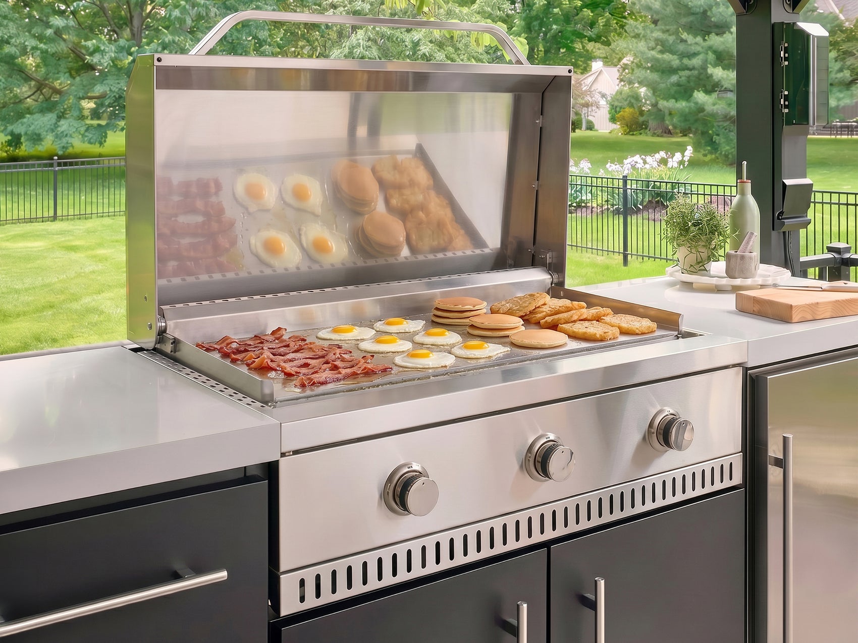 Flat top griddle cooking bacon, eggs, and pancakes on stainless steel in the Lancaster Linear outdoor kitchen.