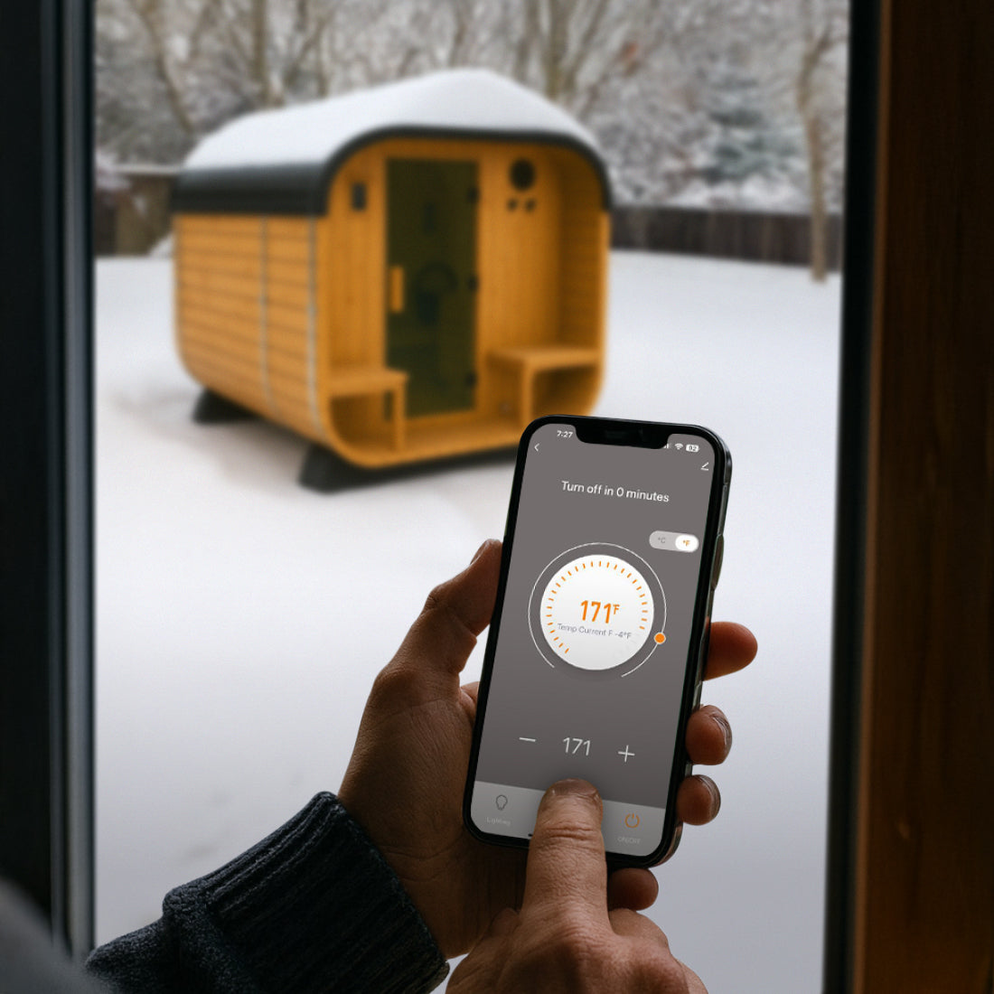 Person inside using Tuya Smart App on smartphone to control Lennon Outdoor Sauna temperature in a snowy outdoor setting