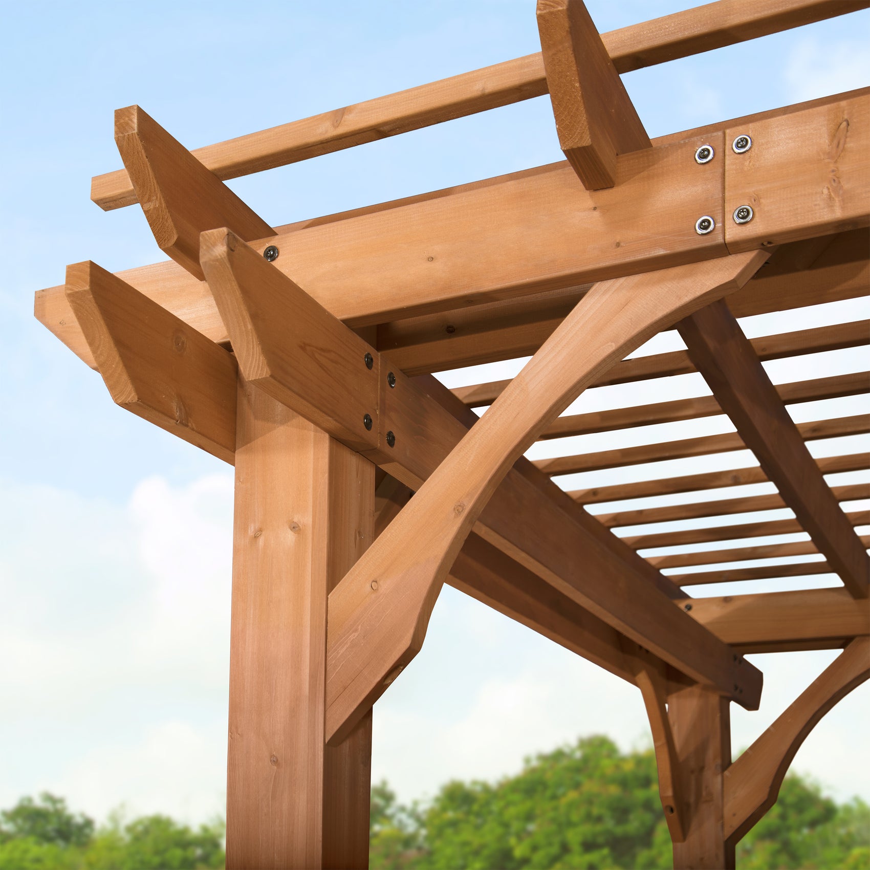 Corner detail of wood pergola showing curved support brackets, decorative joinery, and metal fasteners on crossed beams