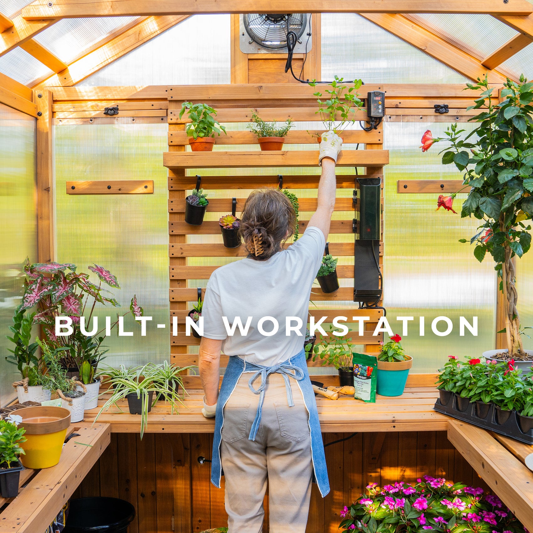 Woman gardening at built-in cedar workstation with vertical slat wall inside the Bellerose home greenhouse kit.