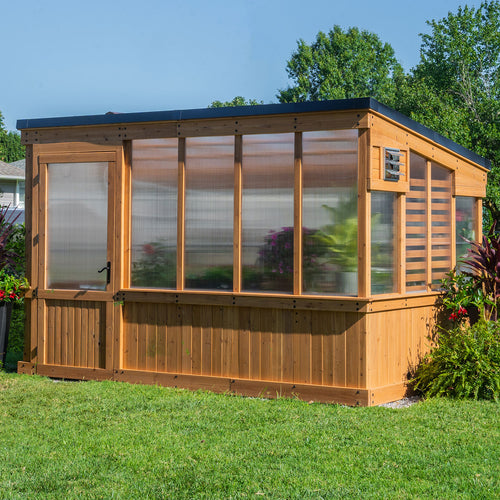 A cedar and polycarbonate Zalie greenhouse with a wide entry door, large front panels, and a side intake vent, set on a lawn.