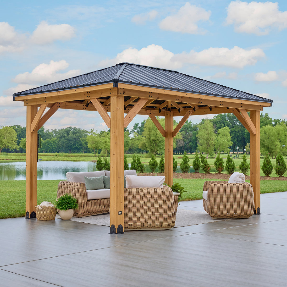 Cedar wood gazebo with a four-sided black steel hip roof, staged with wicker seating on a paved patio.