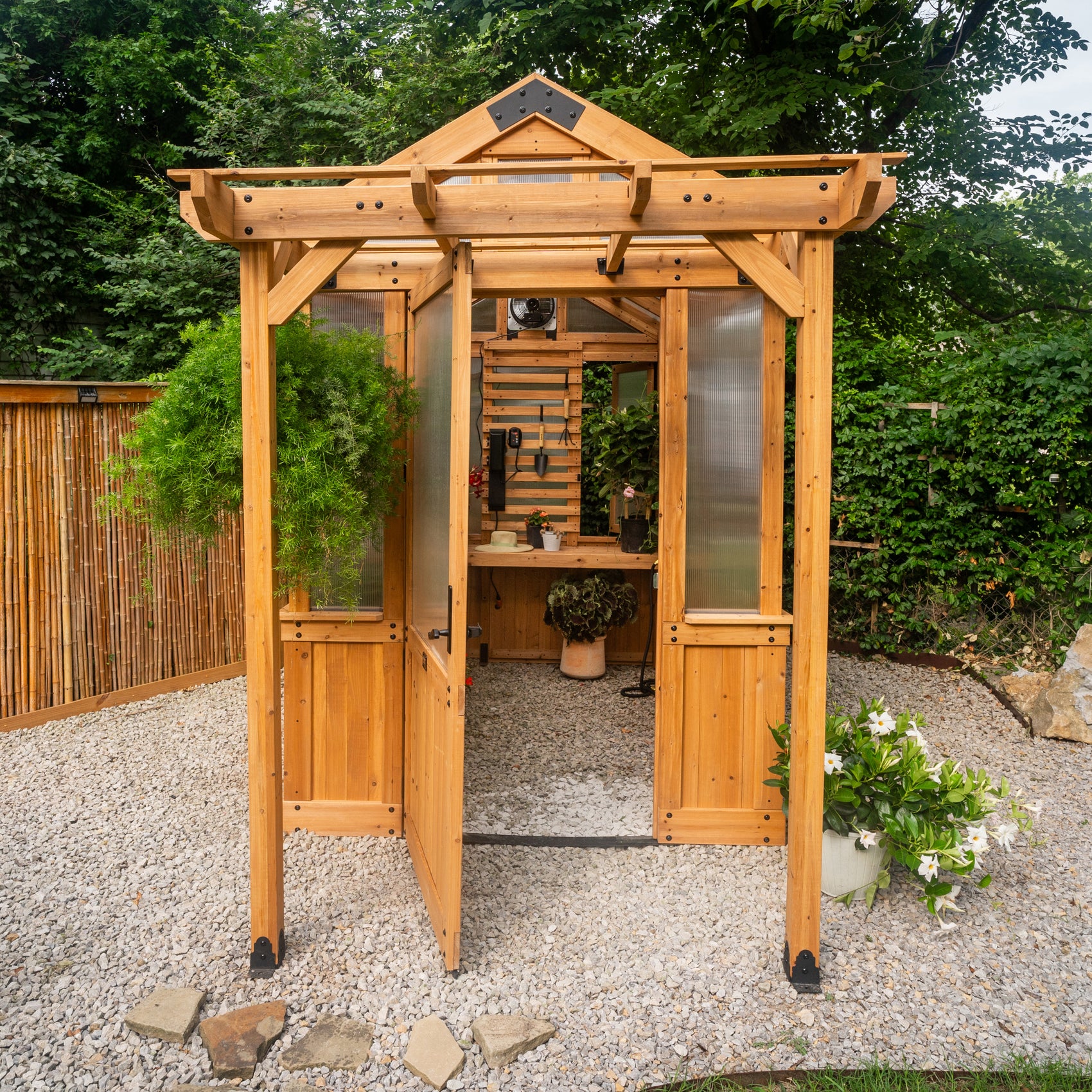 Cedar and polycarbonate Bellerose 9x6 wooden greenhouse with a wide entry door open, staging shelves, and slat wall.