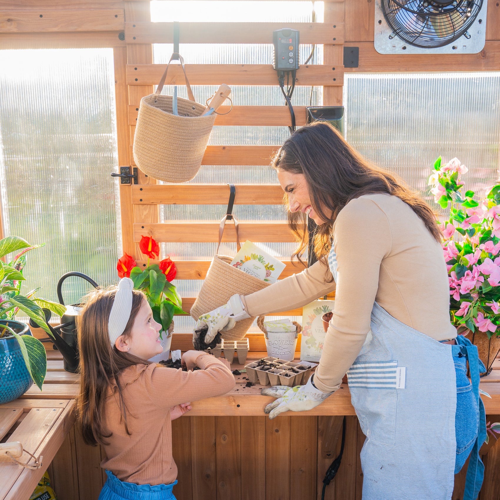 Woman and child starting seeds together in the Willow 9x6 greenhouse kit, filling trays at the cedar staging shelves.