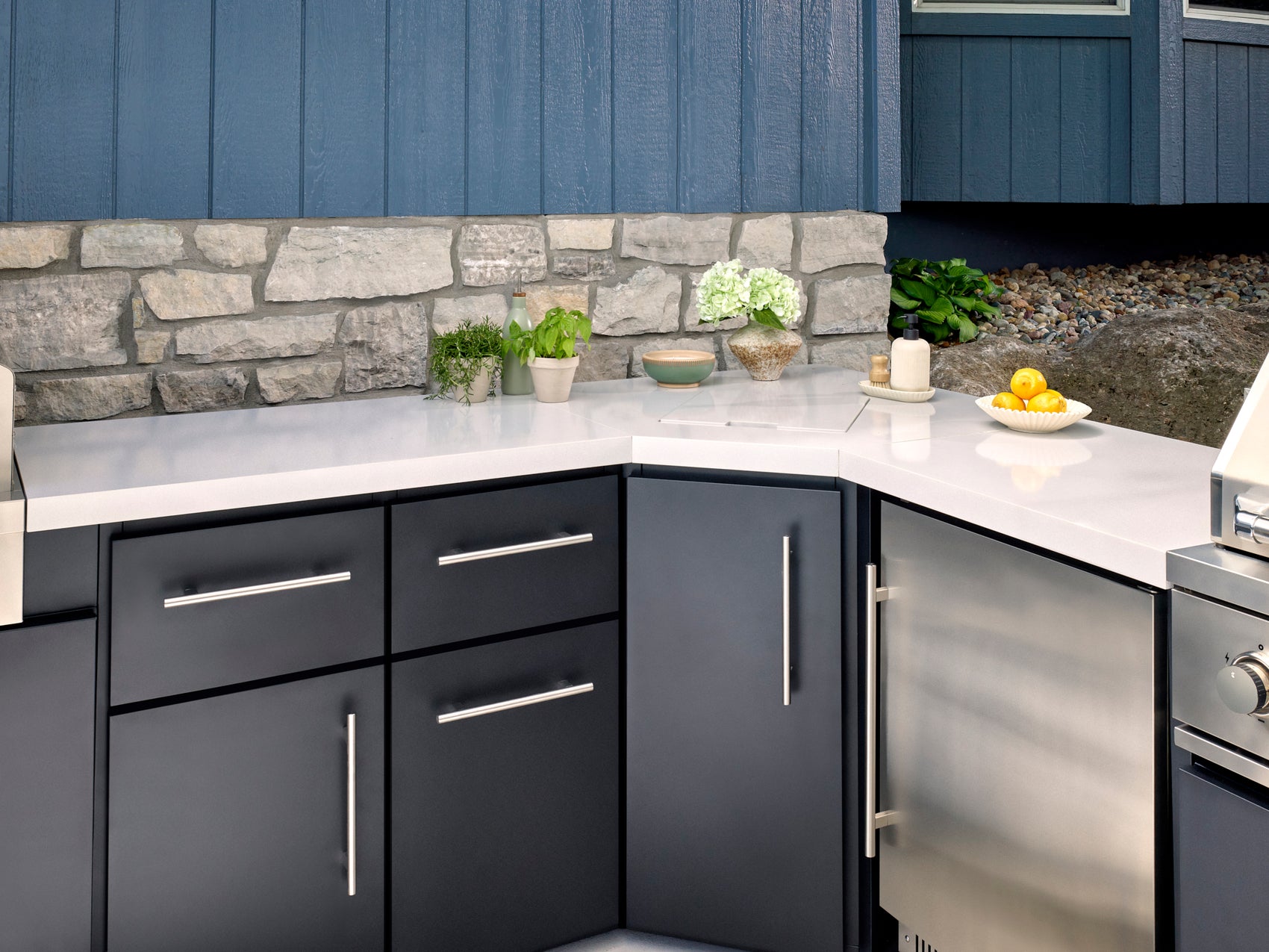 Emory Corner combo outdoor kitchen with engineered stone countertop and dark cabinets on a backyard patio.