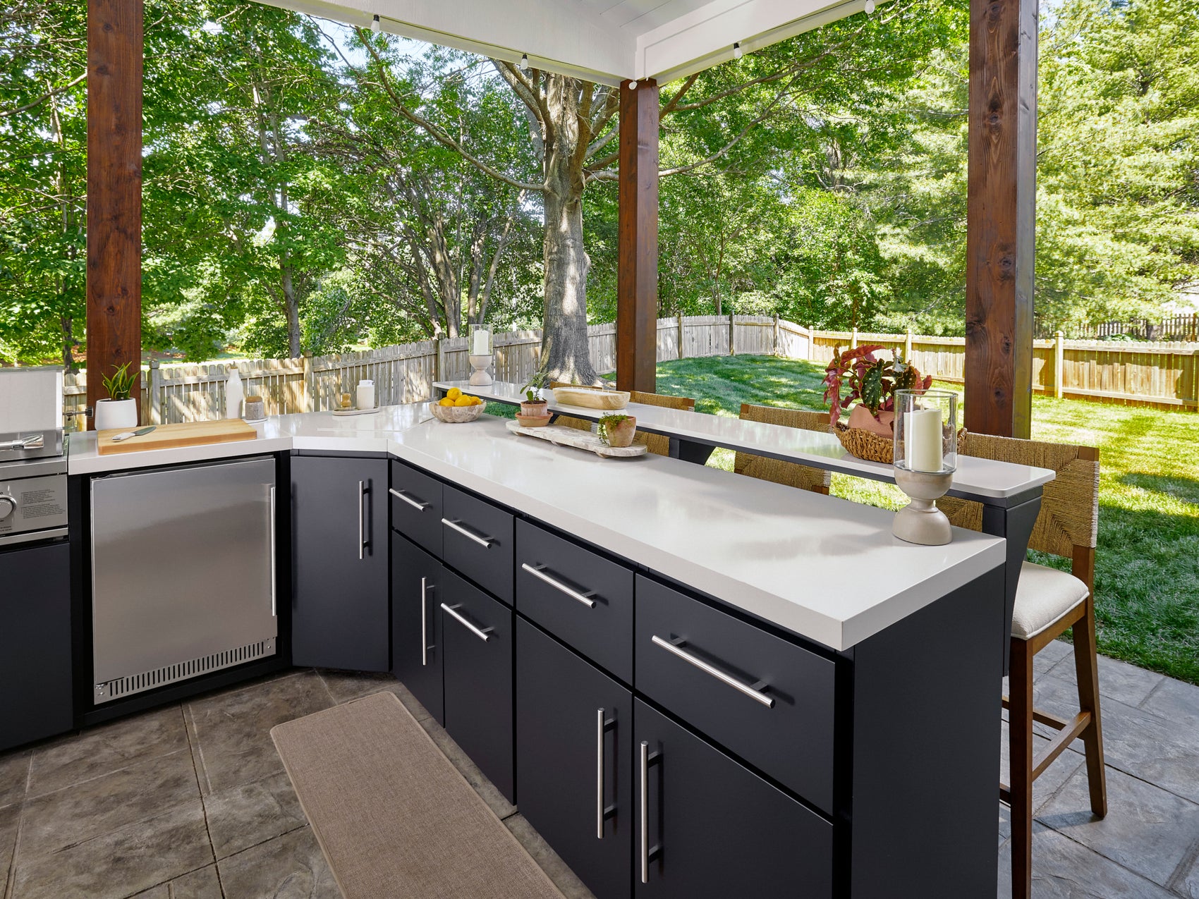 Emory steel kitchen cabinetry with white countertop and stainless refrigerator overlooking tree-filled backyard.
