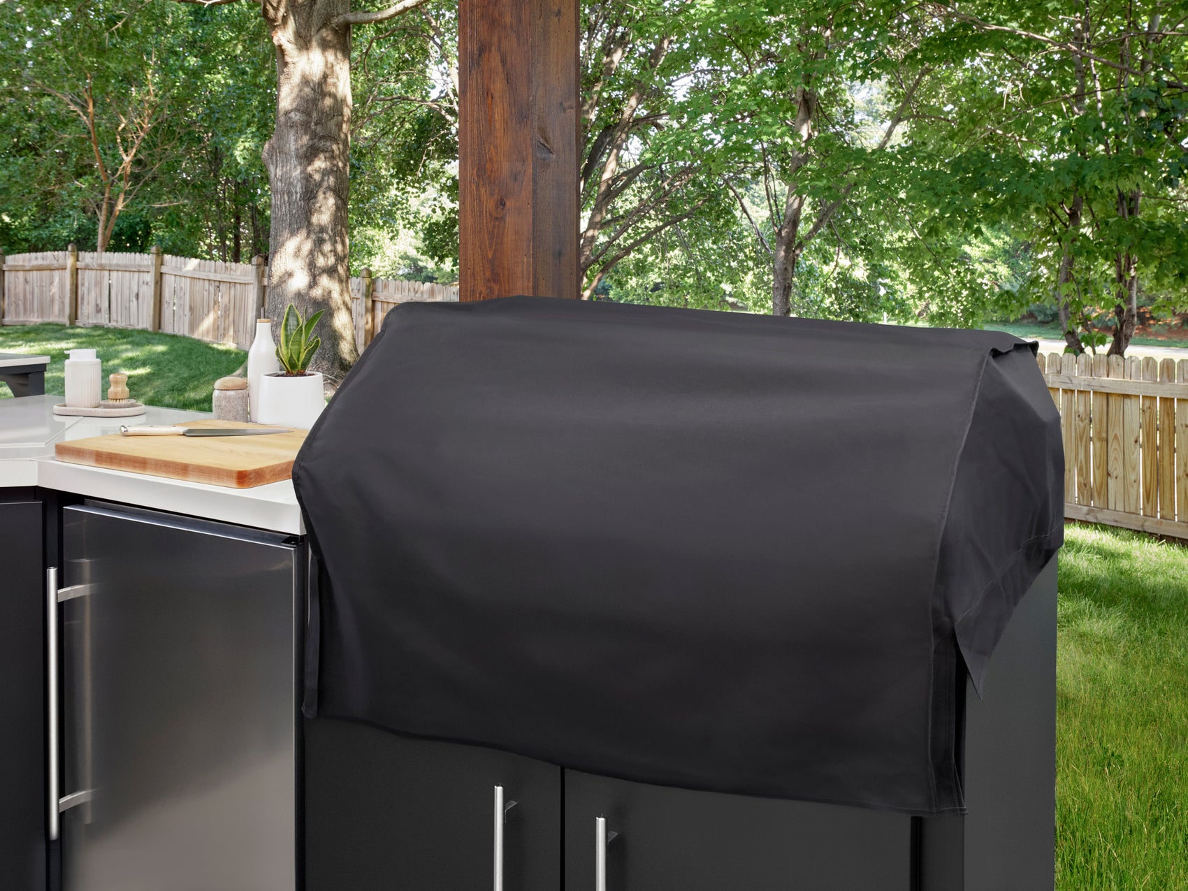 Black protective cover draped over patio grill in Emory backyard outdoor kitchen with engineered stone countertop and trees.