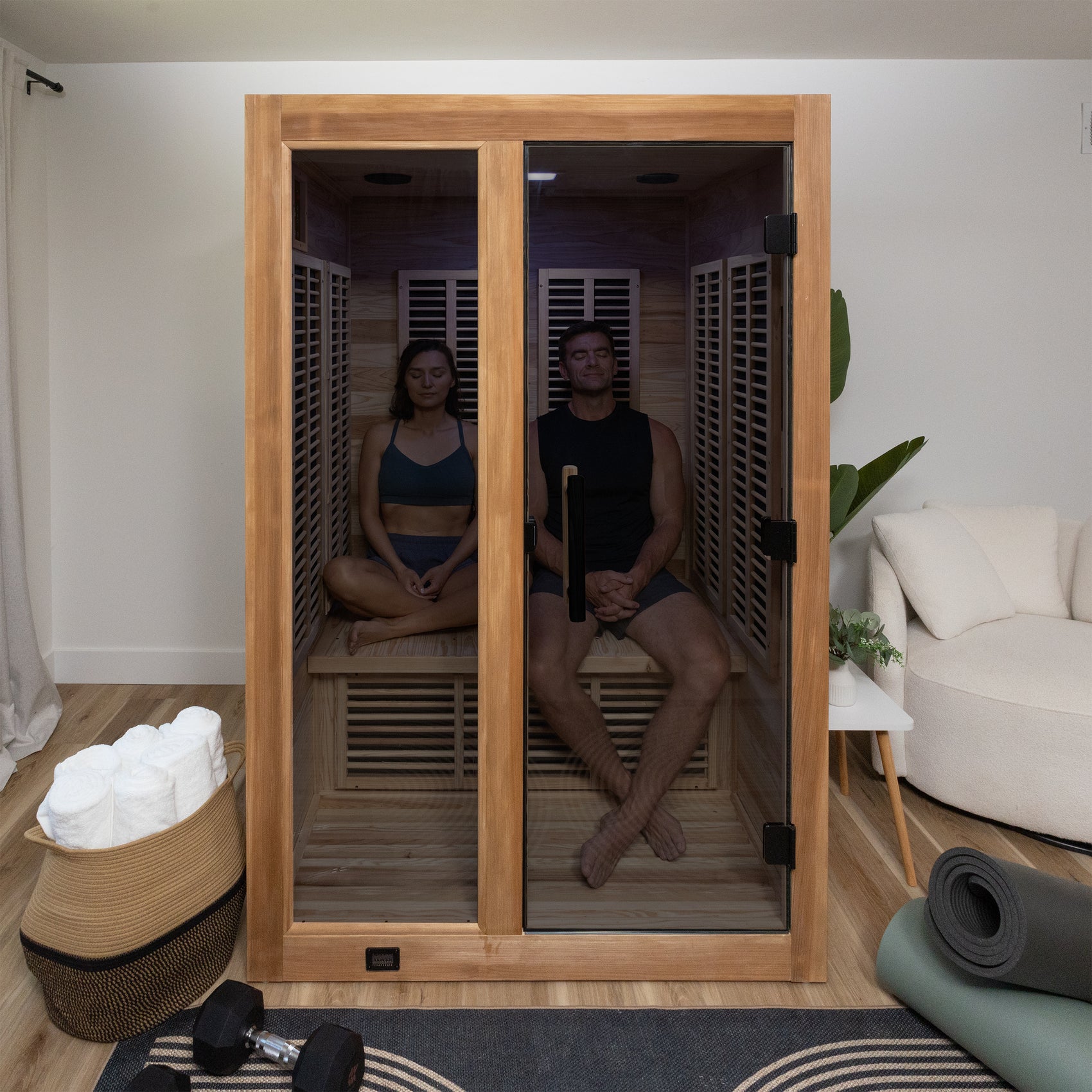 Knox Indoor Infrared Sauna – 2 Person with two people sitting inside a wooden infrared sauna with a modern living room in the background.