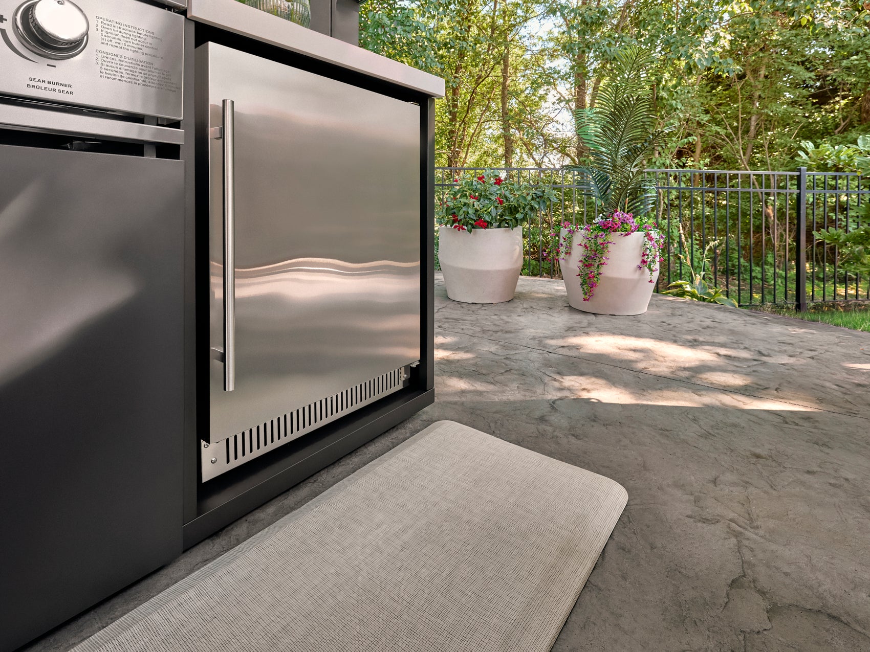 Lancaster galley kitchen with built-in refrigerator on outdoor patio with planters and railing overlooking green wooded area.