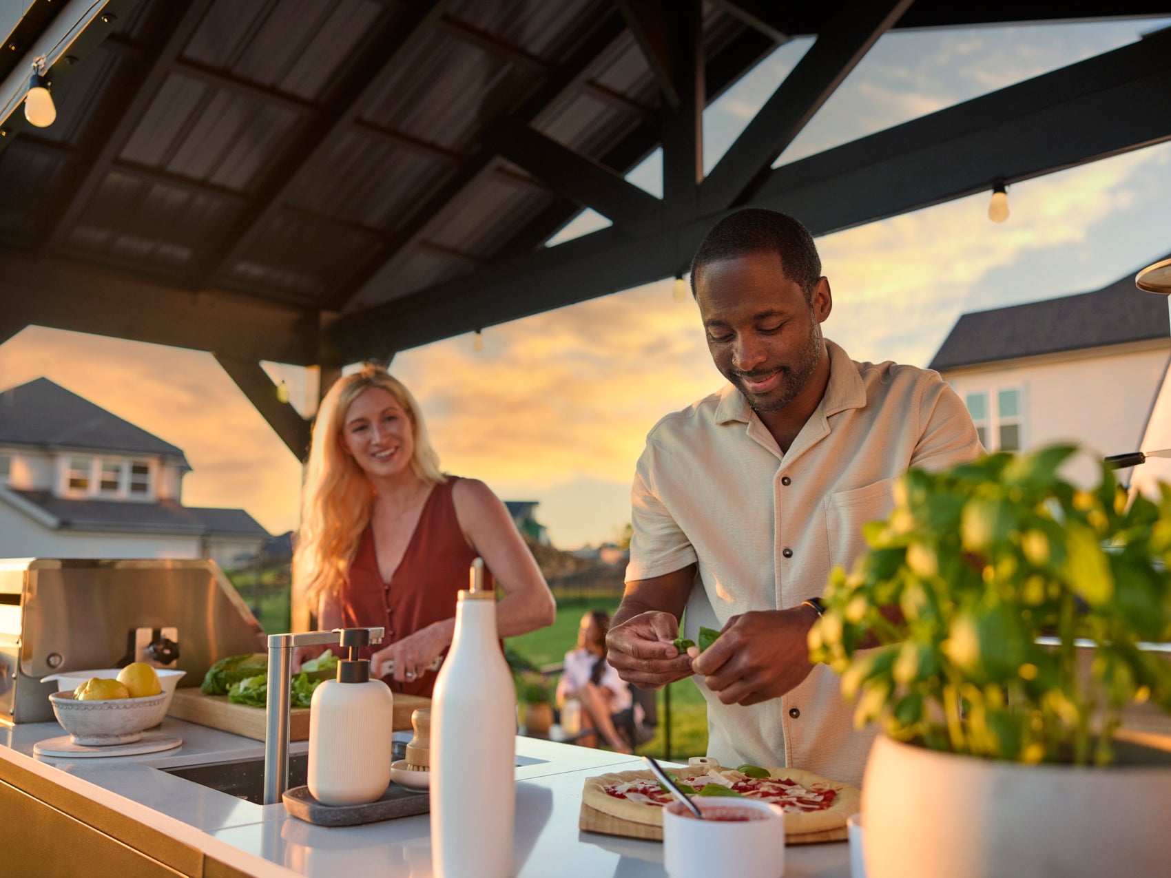 Man grilling at covered backyard kitchen with stainless steel 5-burner grill at sunset