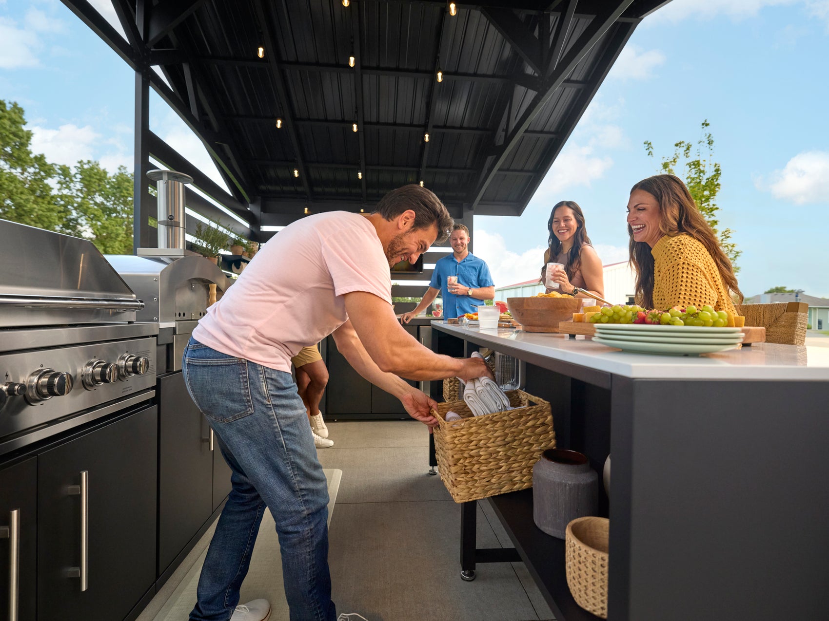 Steel roof shades the Range Outdoor Living kitchen with a built-in grill as a man takes items from a basket.