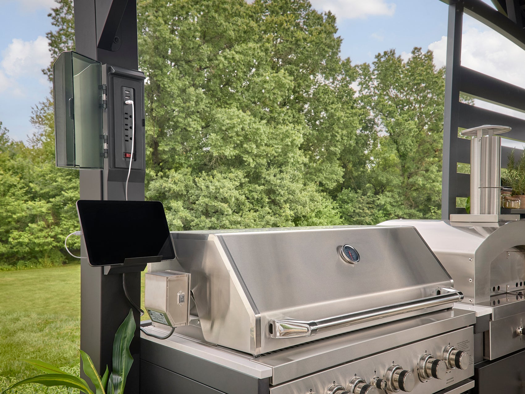 Stainless steel grill with electrical panel mounted on black steel column beneath trellis roof in Langston outdoor kitchen.