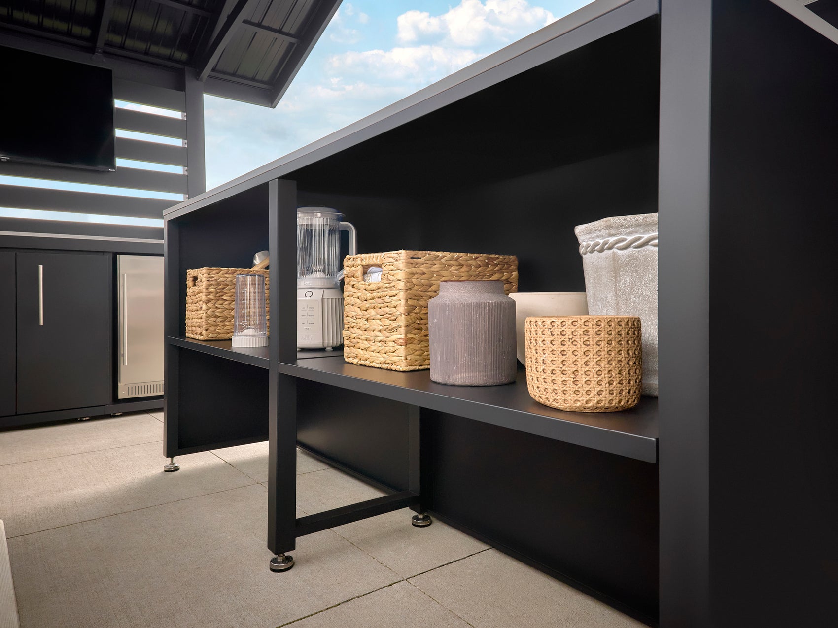 Modern Langston outdoor kitchen with dark storage shelving holding woven baskets and appliances in an outdoor living space.