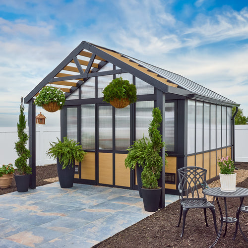The Backyard Discovery Larkspur metal greenhouse with a peaked roof composite wood and polycarbonate panels on a paved foundation.