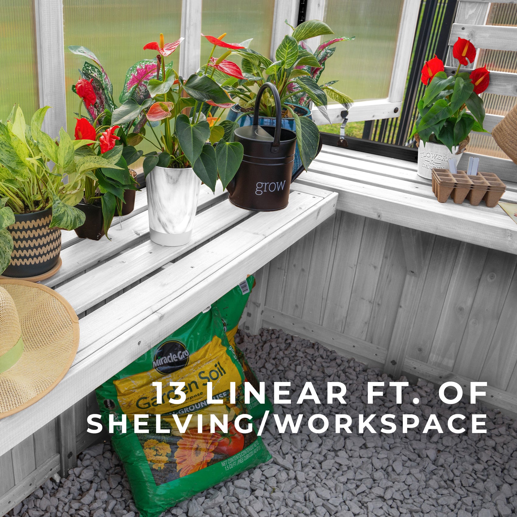 L-shaped staging shelves inside the White Willow greenhouse hold potted plants, a watering can, and a bag of soil.