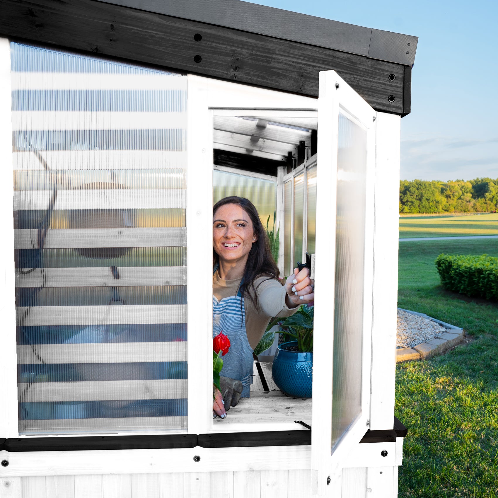 Woman opening an operable window of the White Willow greenhouse for natural airflow.