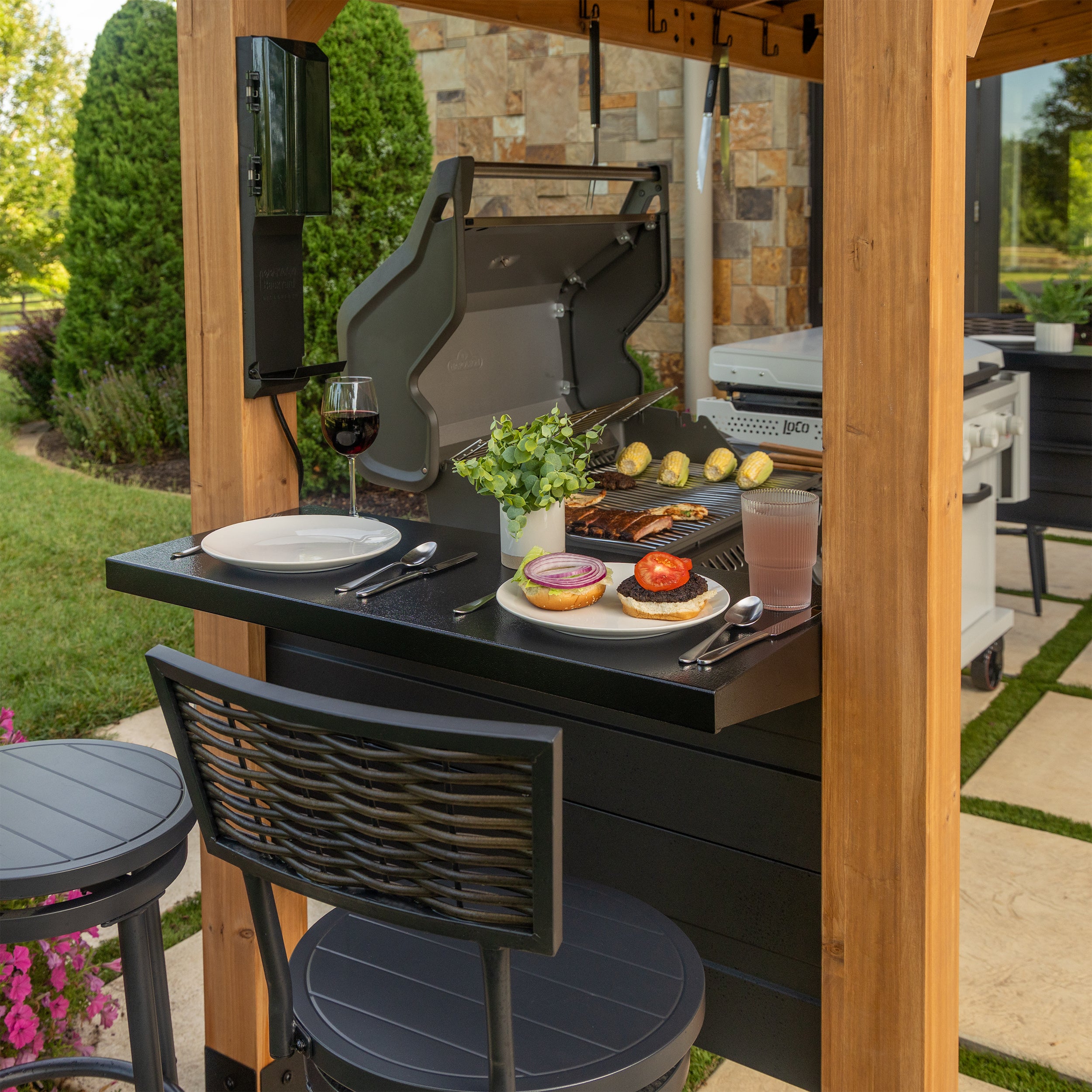 Burger and grilled food served on steel countertop of cedar bbq grill gazebo in backyard patio setting.