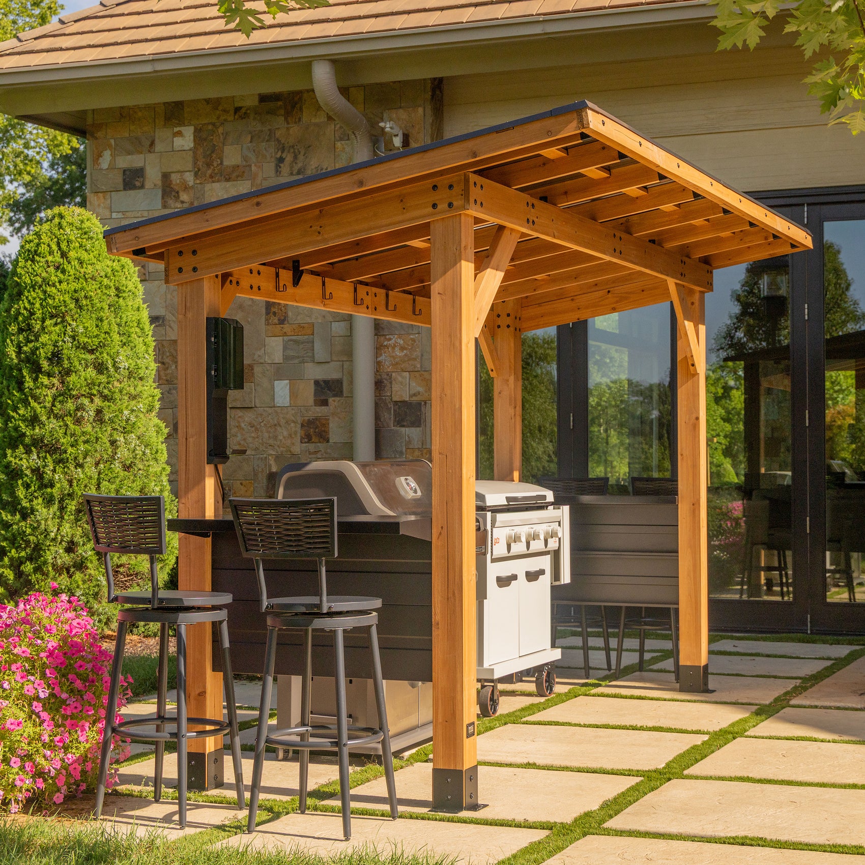 Cedar steel grill gazebo with cantilevered roof, bar countertop, and stools on backyard patio.