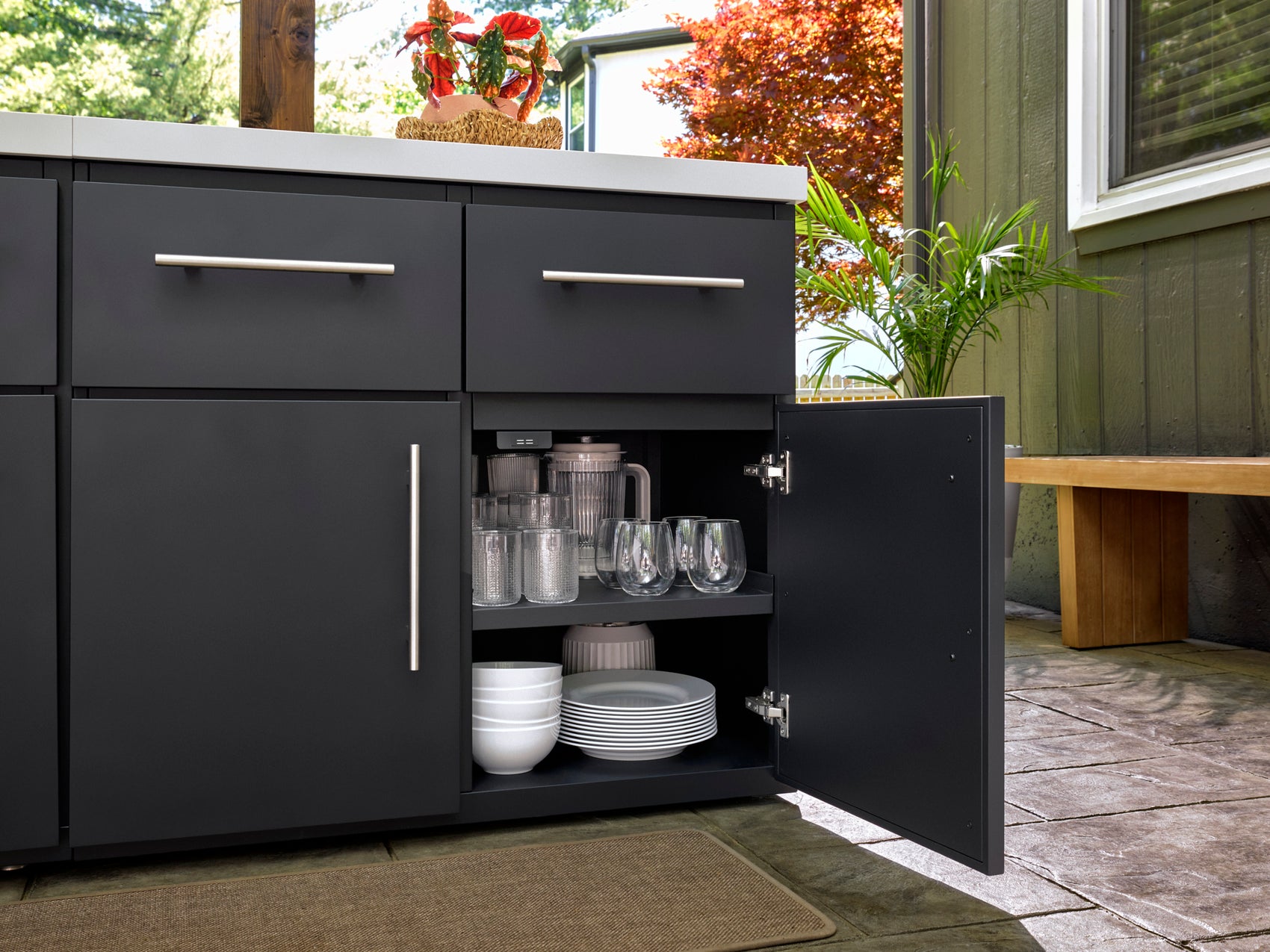 Open black cabinet revealing organized dishes and glassware on interior shelves in Emory outdoor kitchen setting.