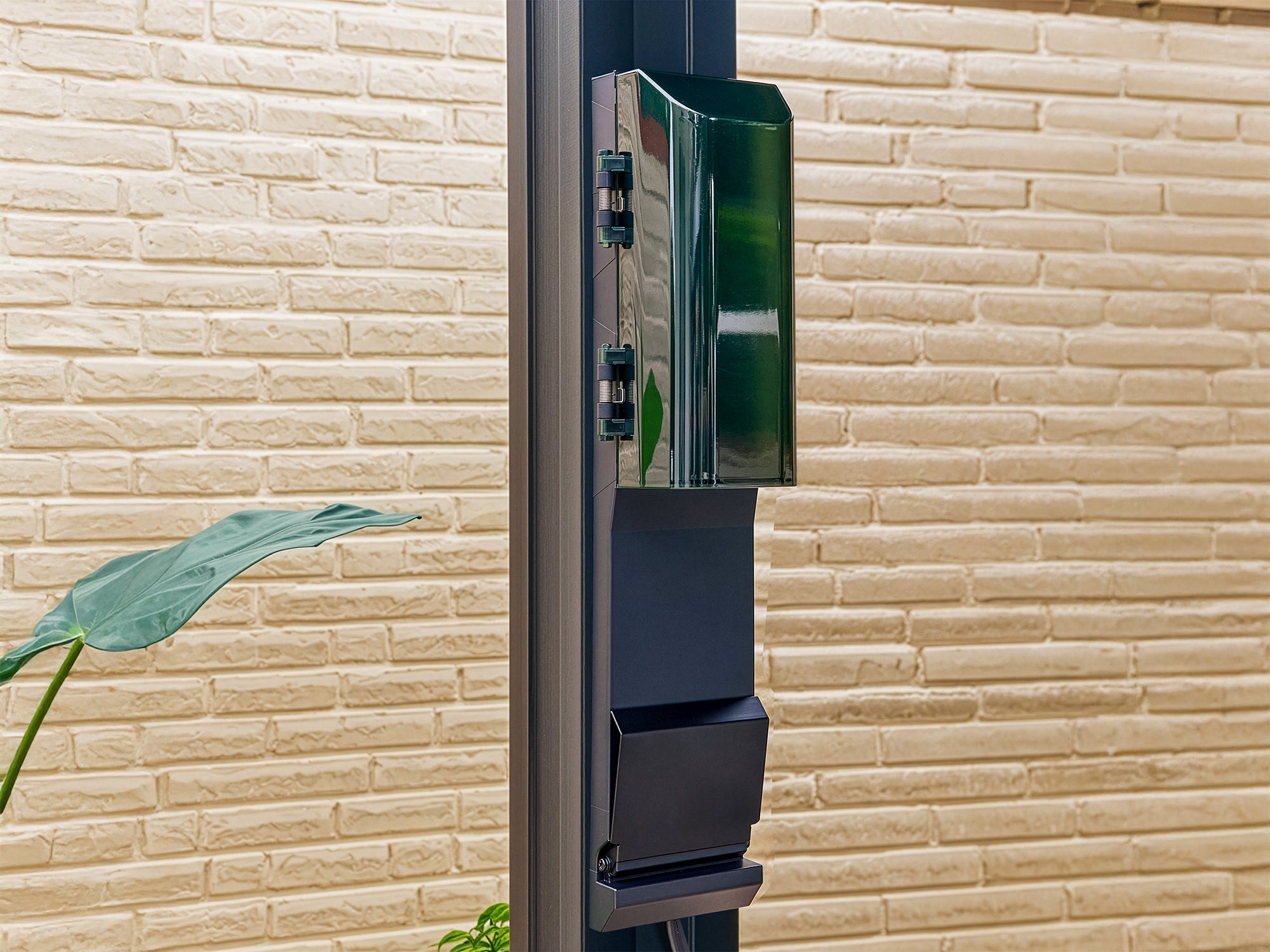 Wall-mounted power outlet with green housing attached to Stratford steel pergola trellis roof post on brick exterior.
