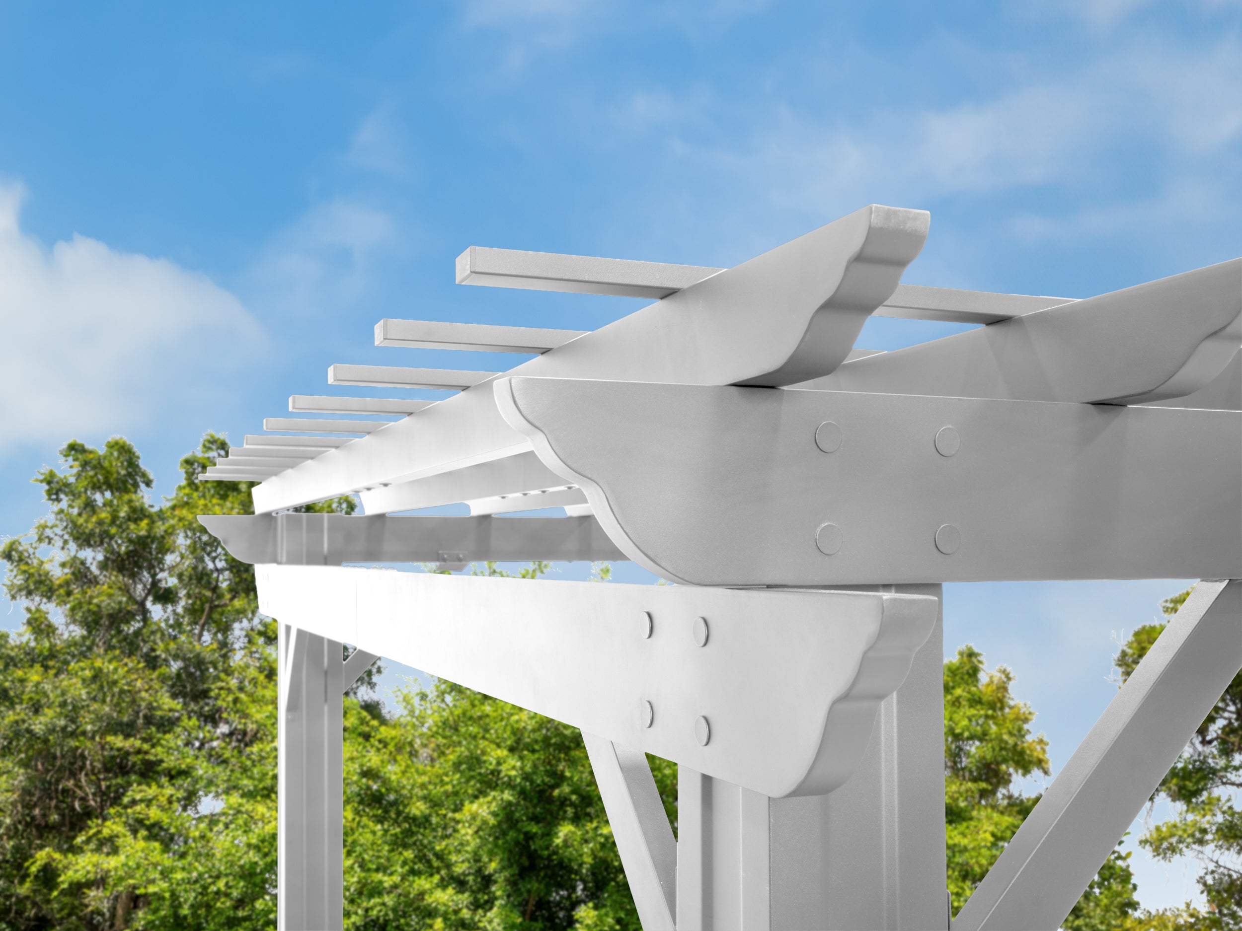Stratford steel pergola hardware connecting white beams and rafters with visible bolt fasteners against blue sky.