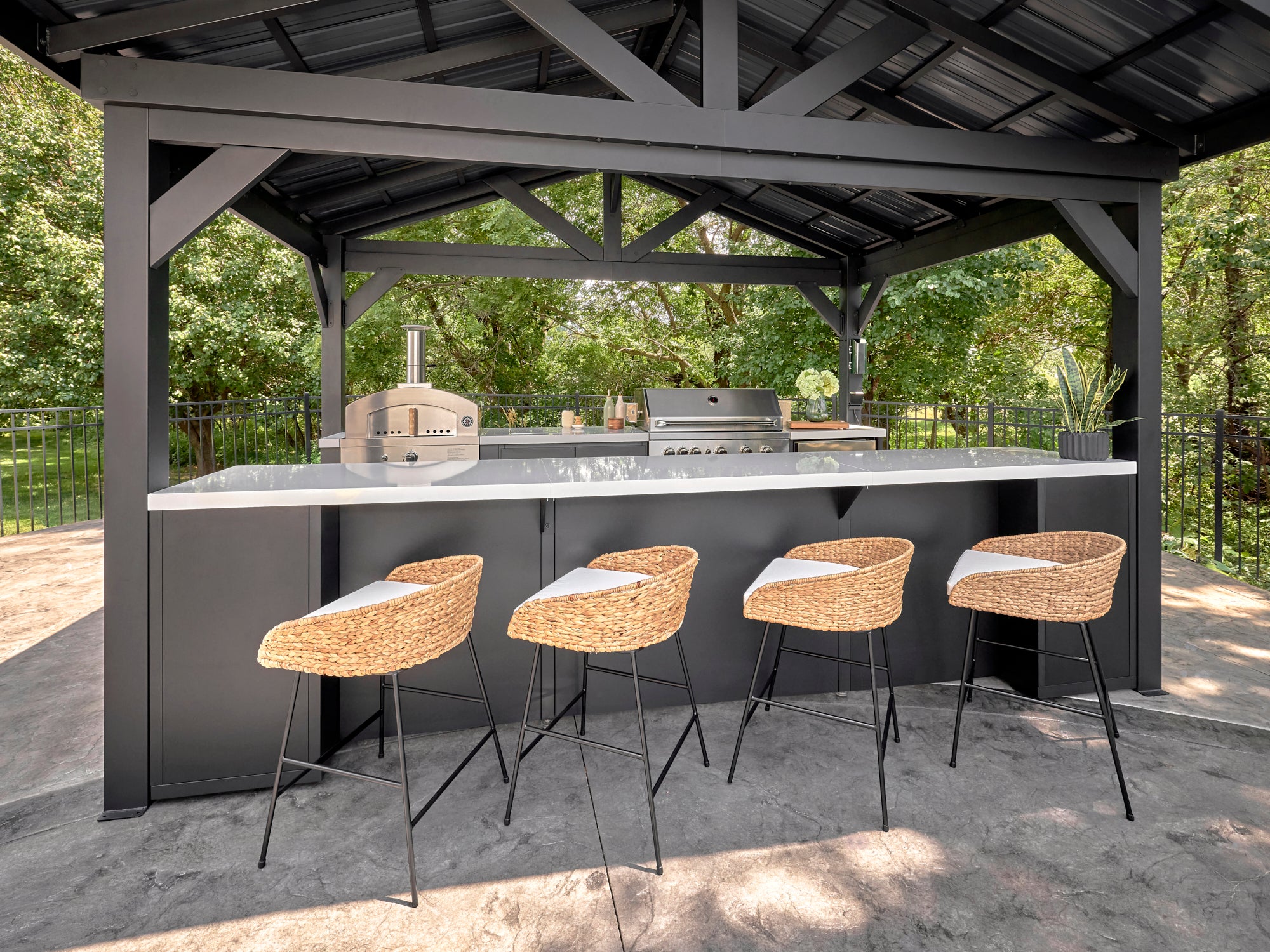 Lancaster outdoor kitchen with built-in backyard bar, bar stools, engineered stone countertop, steel grill and pizza oven.