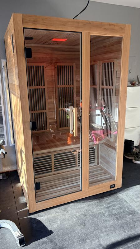 Infrared sauna with wooden exterior and glass door in a room setting.