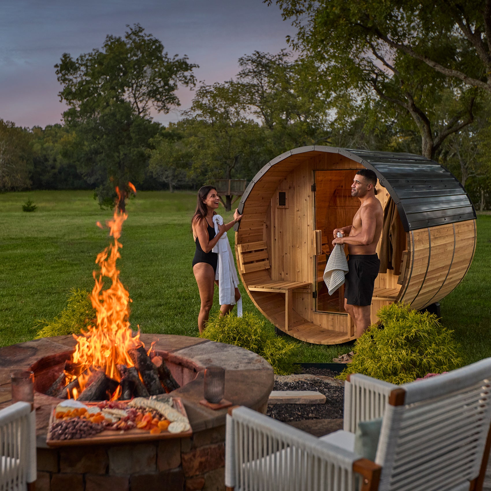 Two people next to Paxton 2-4 person outdoor barrel sauna in backyard setting