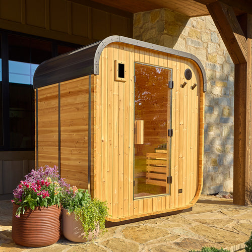 Backyard Discovery Lennon 2-4 person outdoor cube cedar sauna with steel roof on stone patio beside home