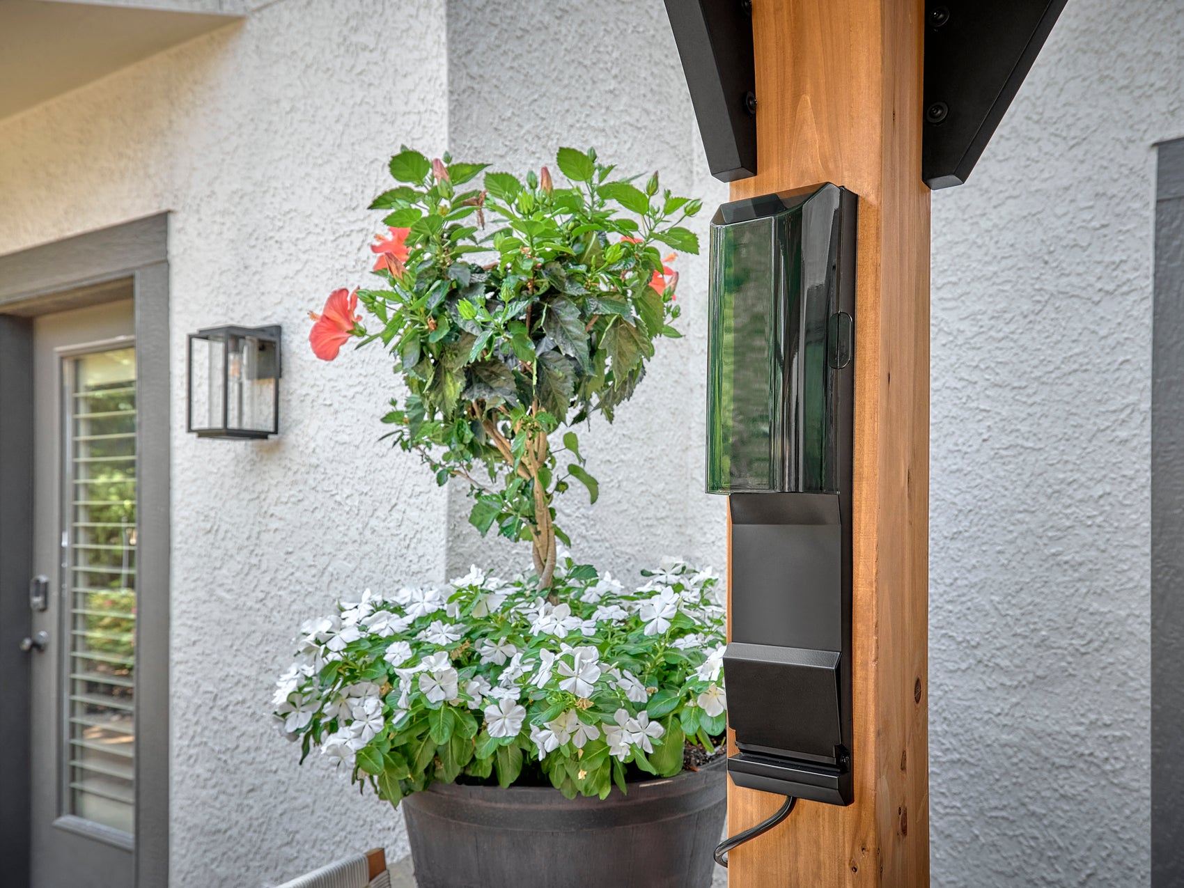 Electrical outlet box mounted on wooden post of Lodge metal gazebo with potted plants and white stucco wall in background.