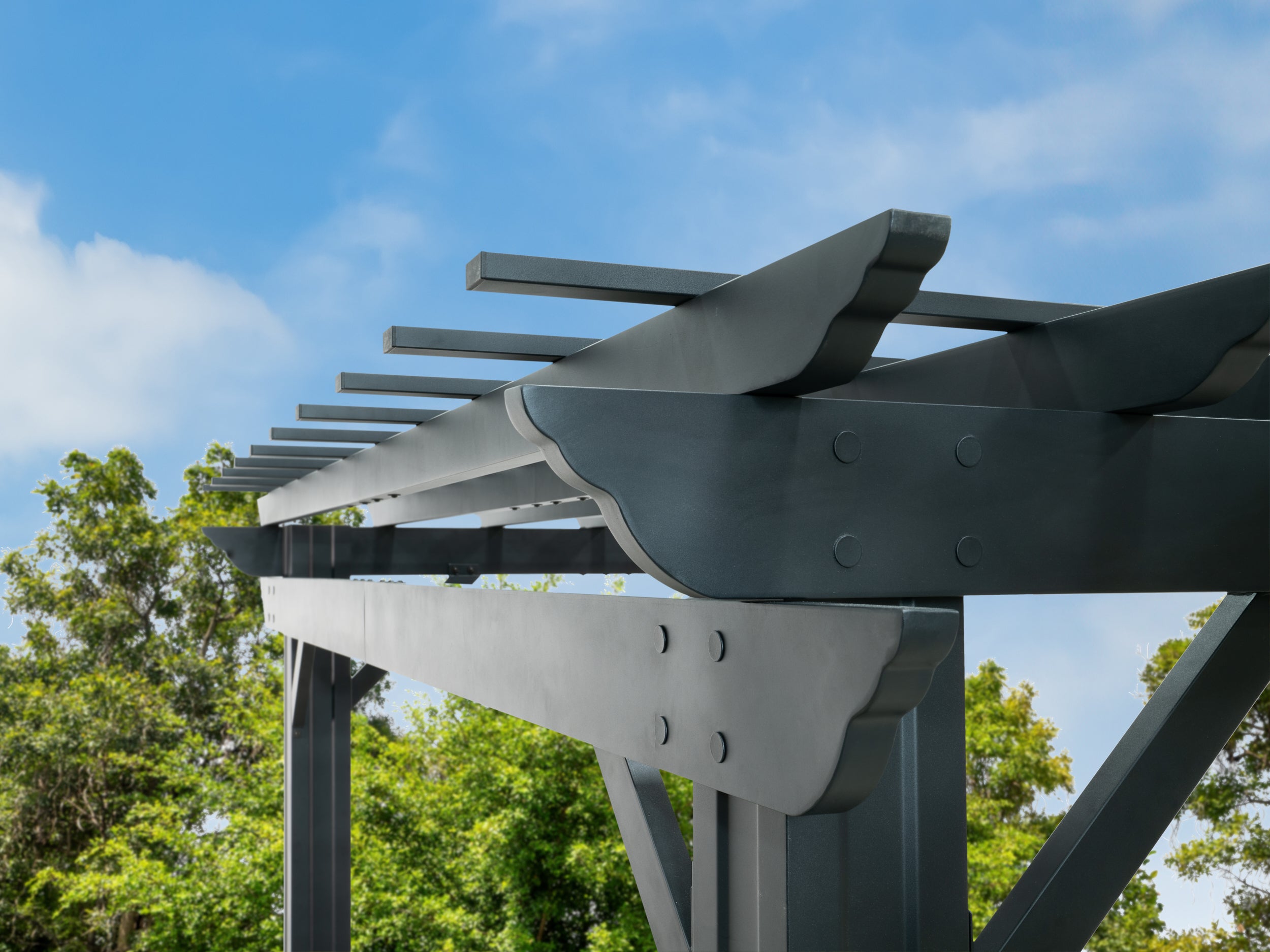 Bolted steel joint connecting curved support bracket to Stratford pergola post with trellis roof rafters above.