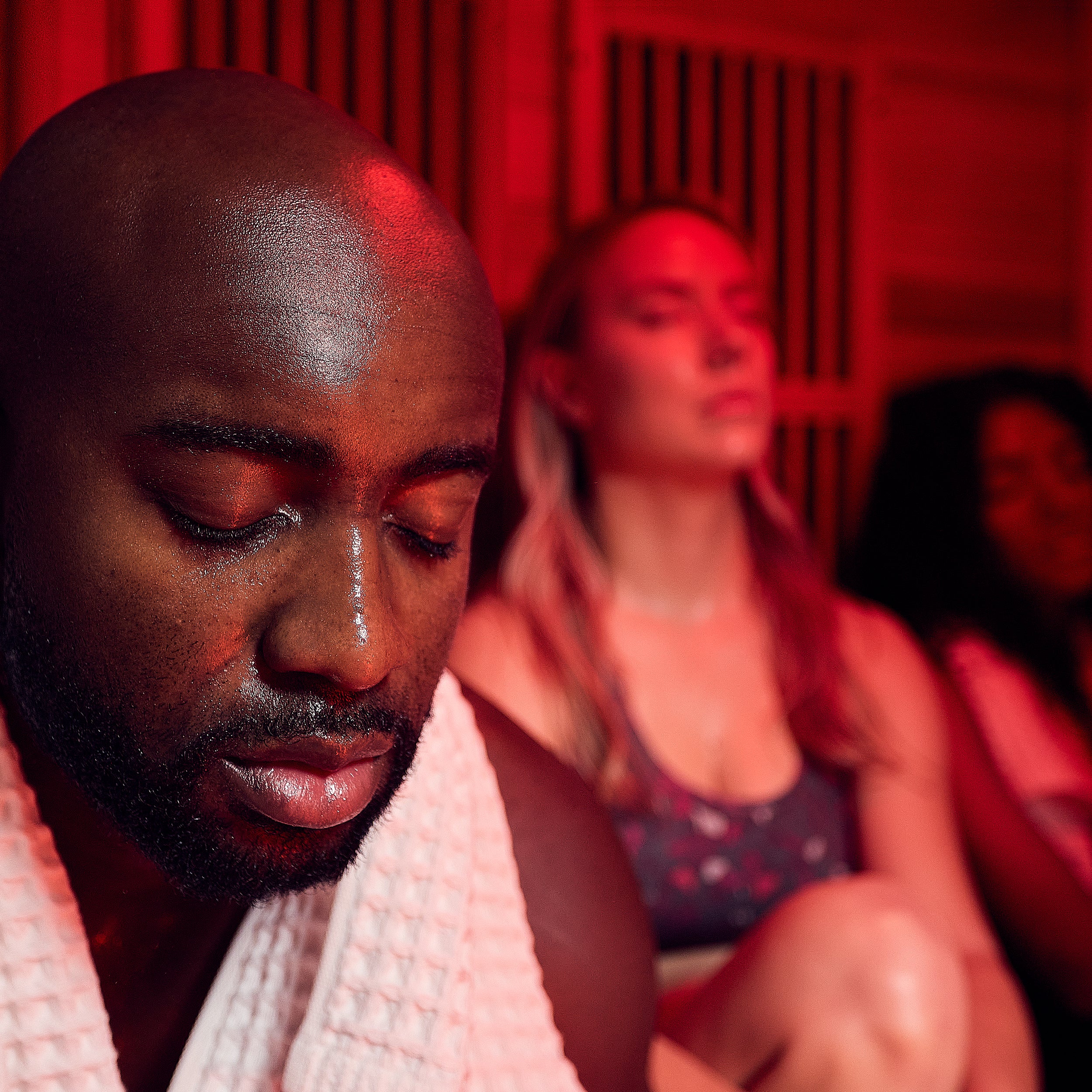 Man sweating with eyes closed during infrared corner sauna session with red light therapy for wellness benefits