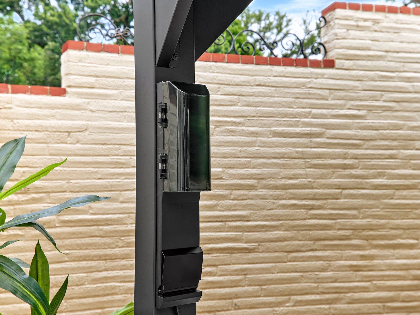 Black power port with electrical outlets mounted on Lancaster steel gazebo post against textured stone wall with greenery.