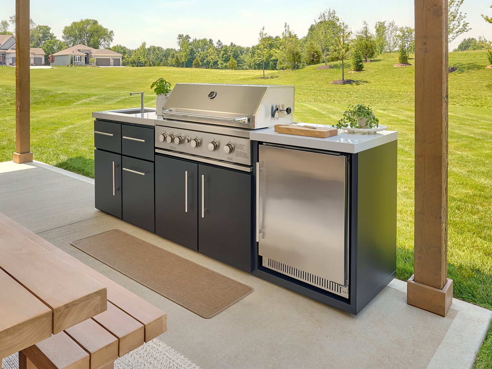 Range Outdoor Living Emory kitchen island with built-in grill and refrigerator on covered patio with lawn view.
