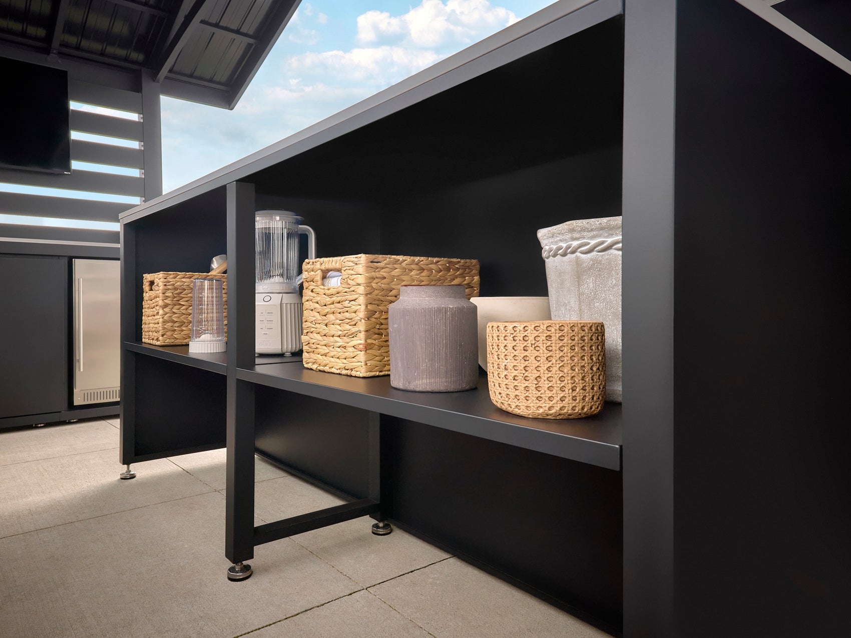 Dark steel storage shelf with woven baskets and blender under Range Outdoor Living Langston steel kitchen.