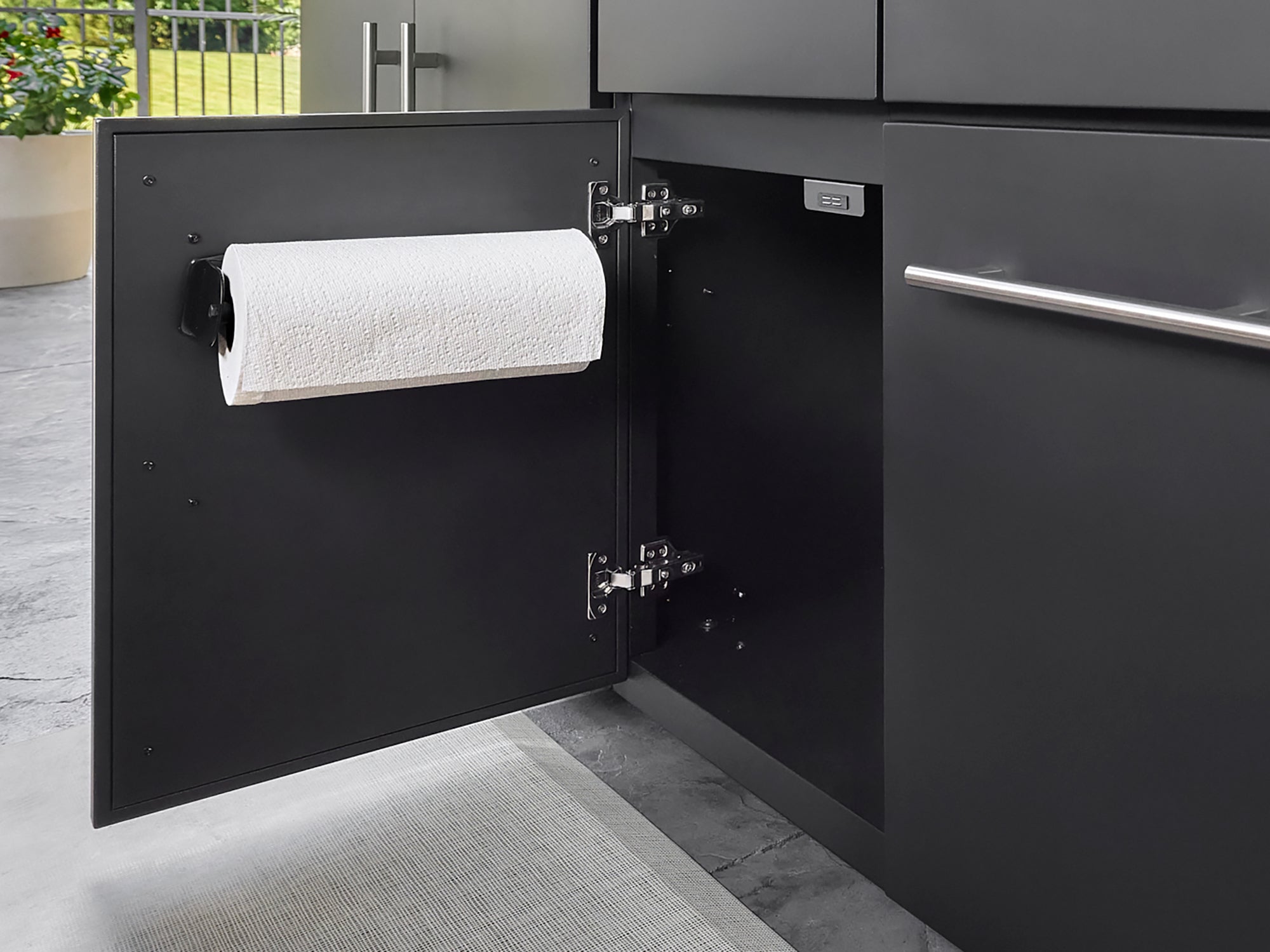 Paper towel holder mounted inside Lancaster outdoor kitchen cabinet door with dark powder-coated finish.