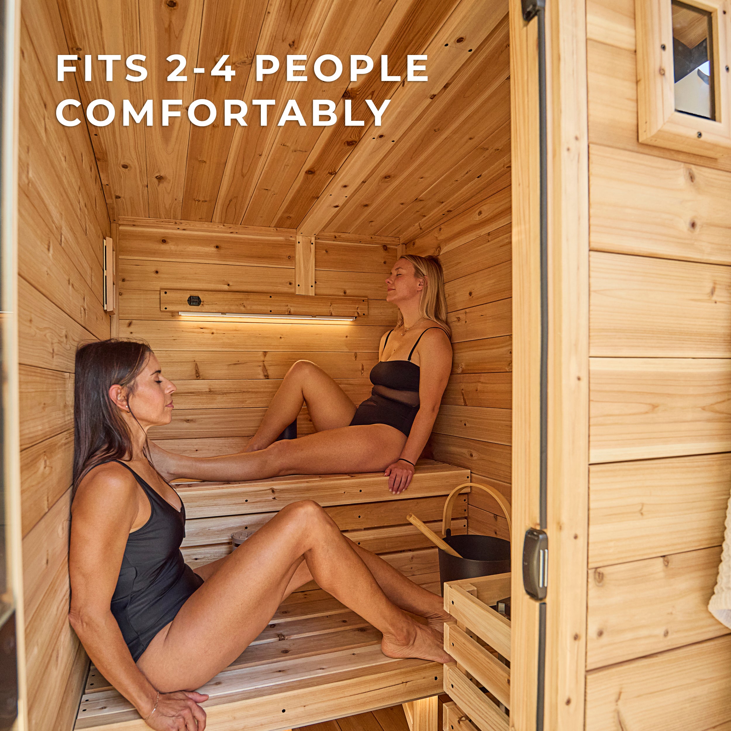 Two people relaxing on tiered cedar benches inside the Henley 2-4 person traditional cedar cabin sauna