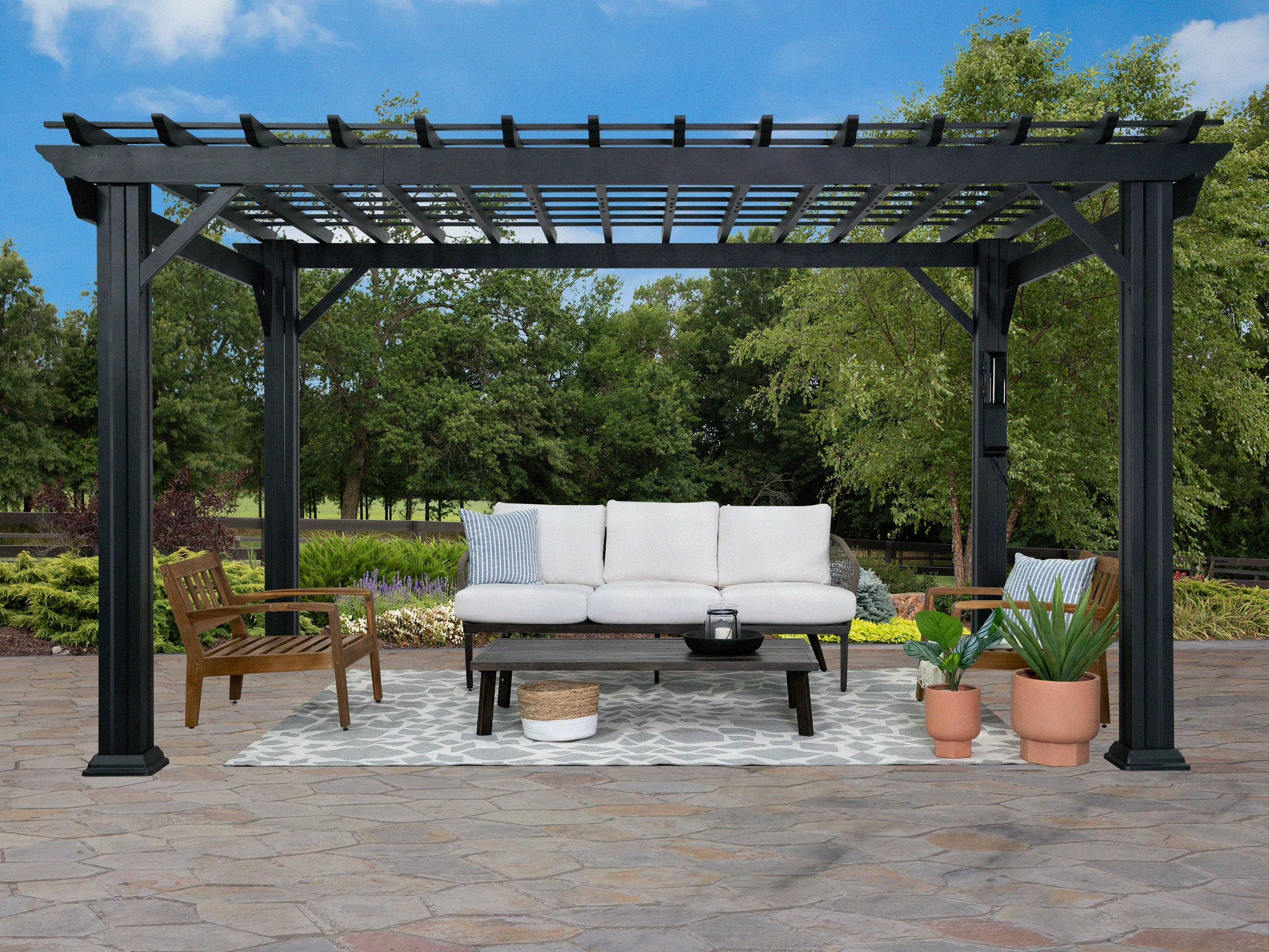 Black powder-coated steel Stratford covered pergola with trellis roof over outdoor sofa seating area on paver patio.