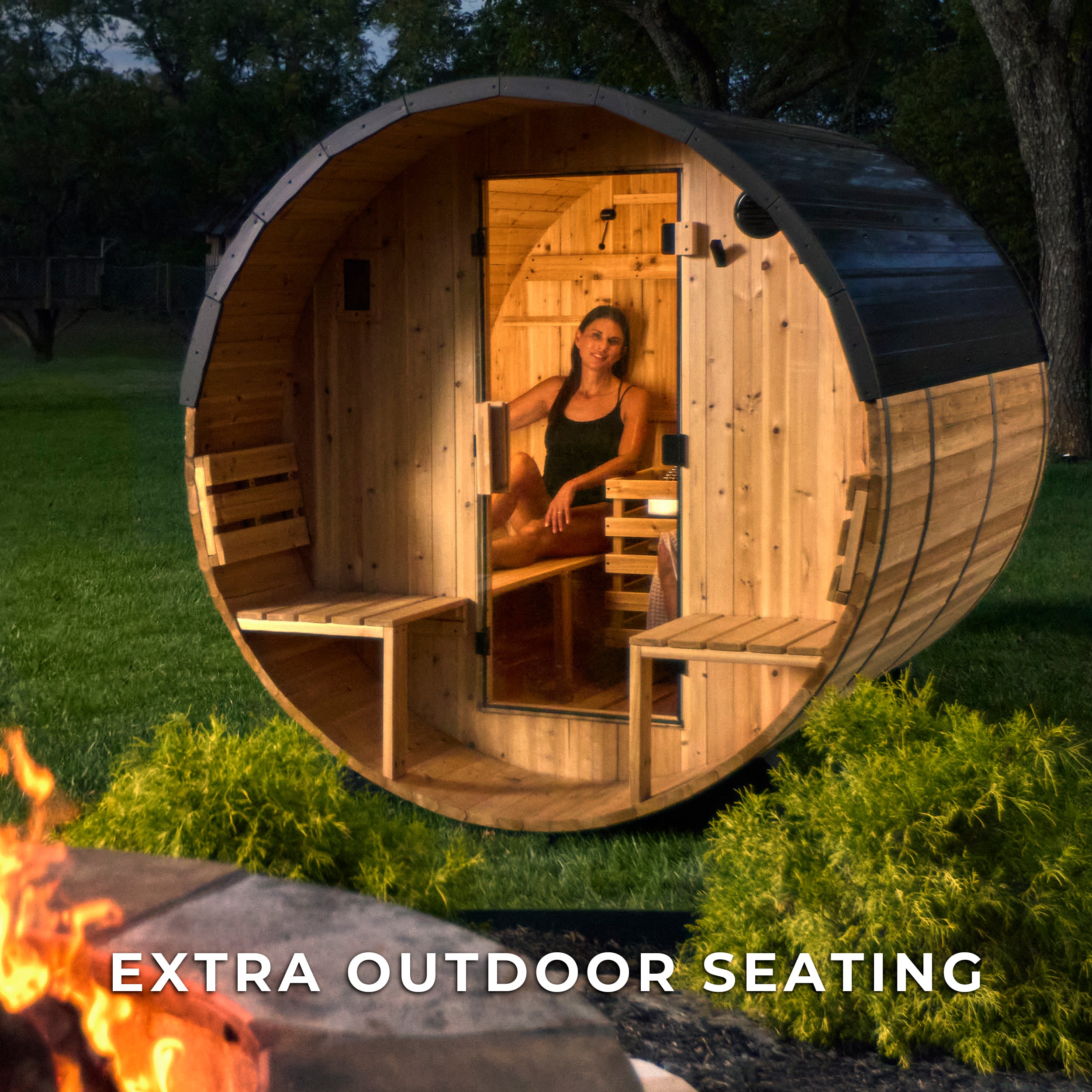 Woman relaxing inside Paxton outdoor cedar barrel sauna at dusk with fire pit in foreground for backyard wellness