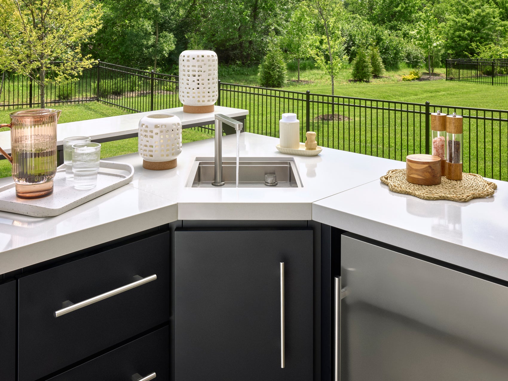 Emory Outdoor sink station with modern faucet and built-in basin on white engineered stone counter with dark cabinetry below.