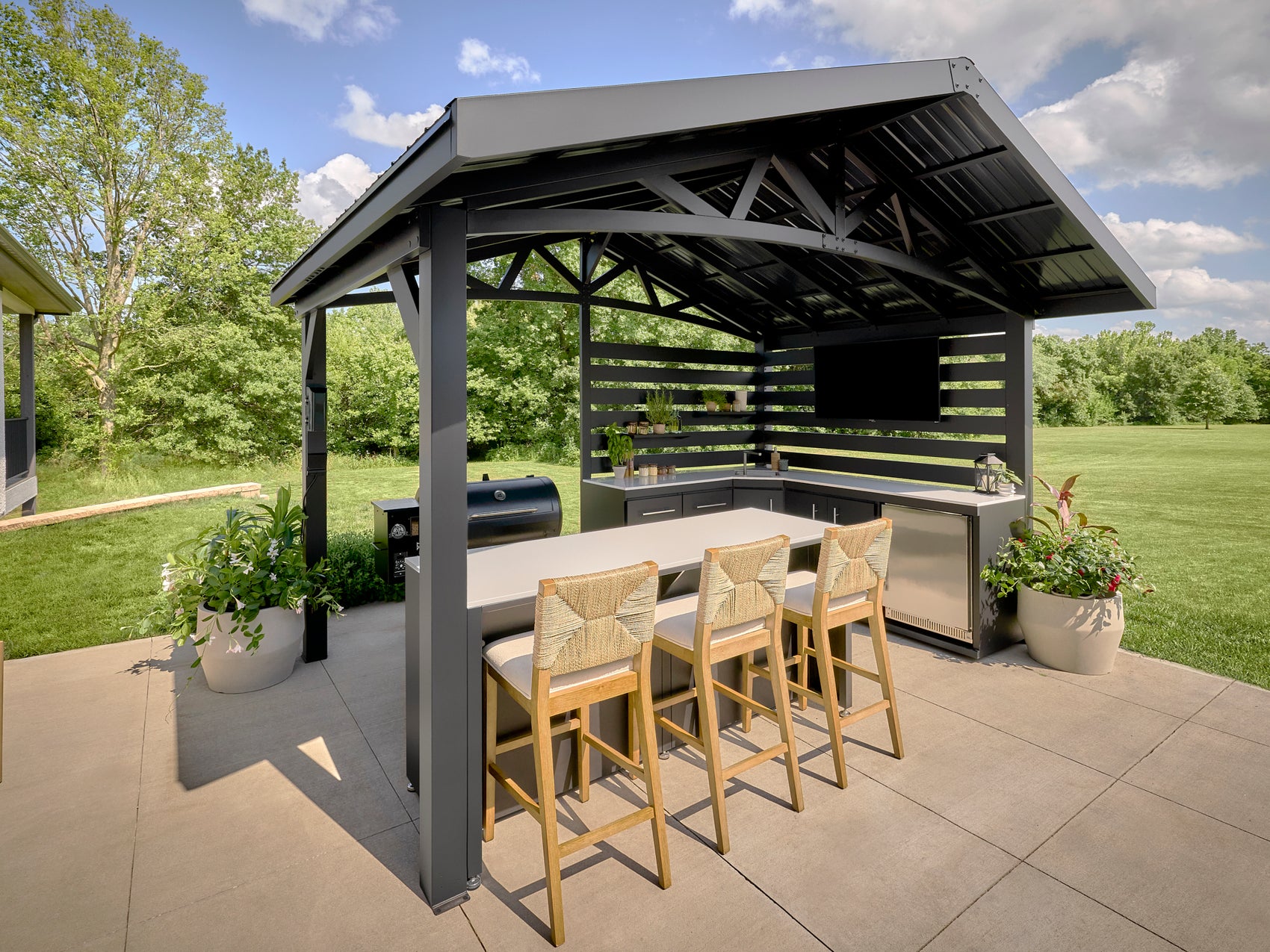 Modern steel roof covering Langston outdoor kitchen with bar seating and grill in spacious backyard setting.