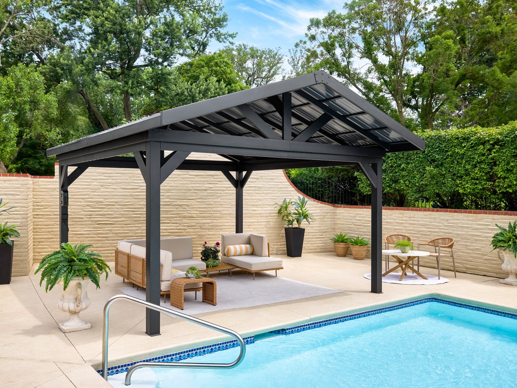 Lancaster steel gazebo with roof sheltering poolside lounge area with modern outdoor furniture and privacy fence in backyard.