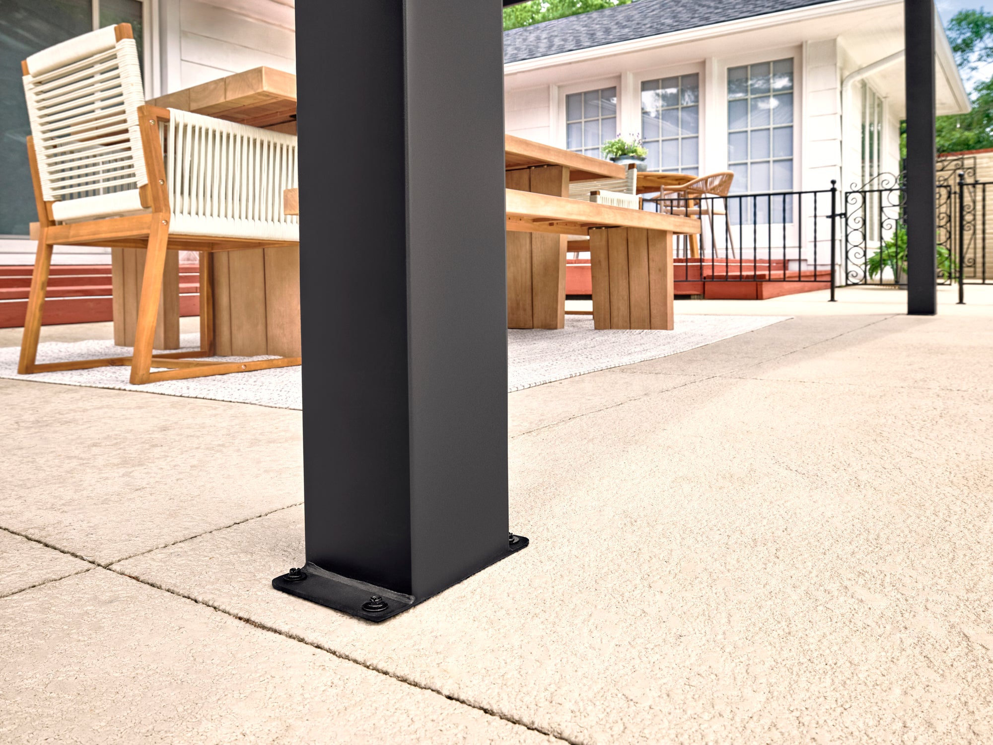 Black steel support post with mounting bracket on concrete patio Lancaster beneath gazebo roof with wooden table and chairs.