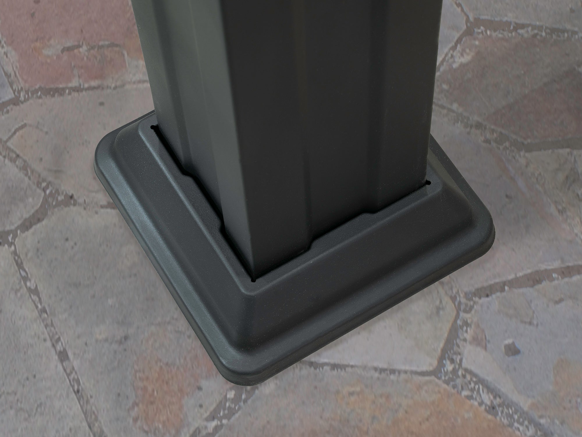Dark gray powder-coated steel post with matching base plate, part of Stratford pergola hardware system, on brick patio.